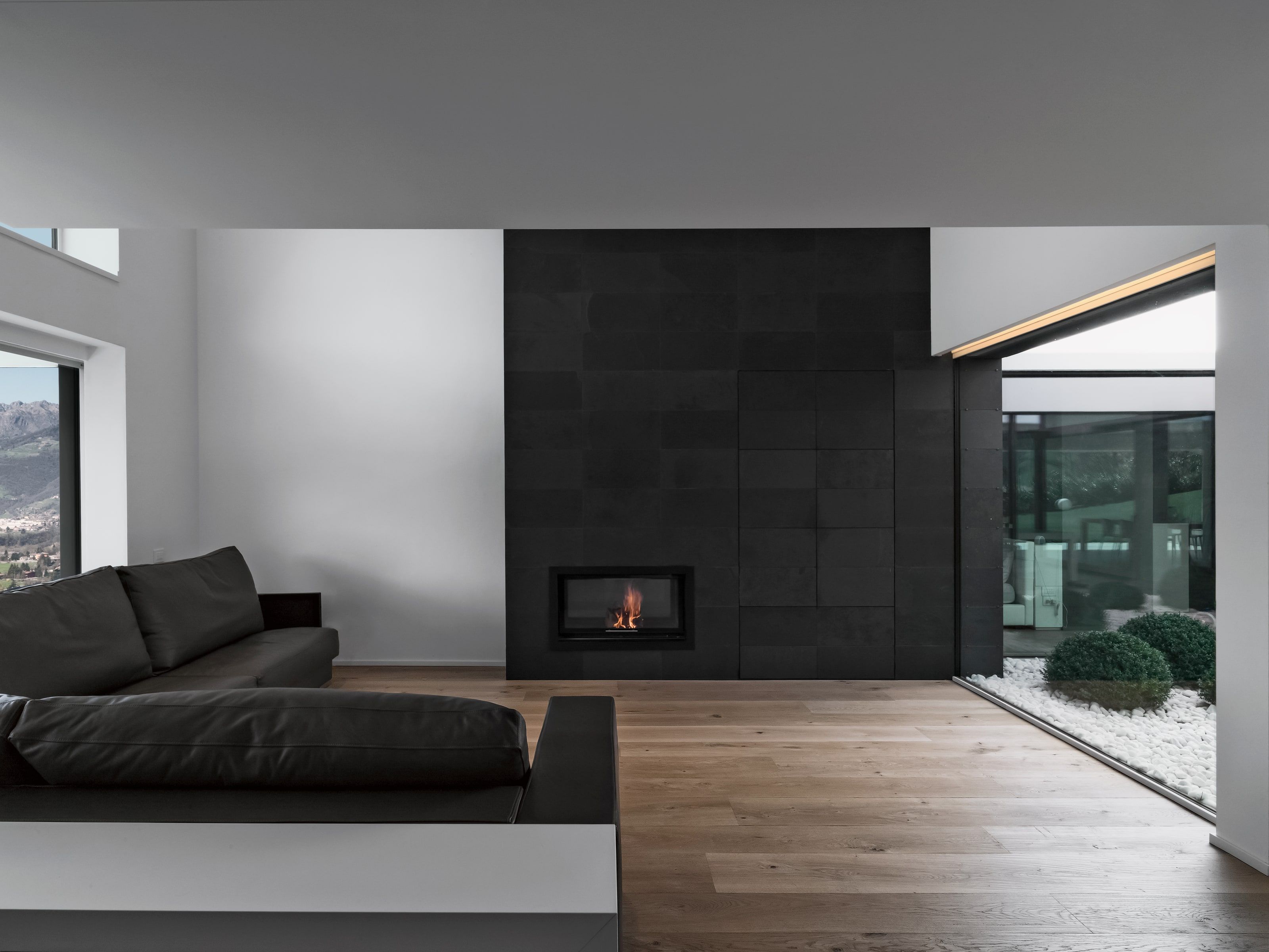 Moderner Wohnraum mit dunkler Kaminwand, Holzboden und großen Fenstern