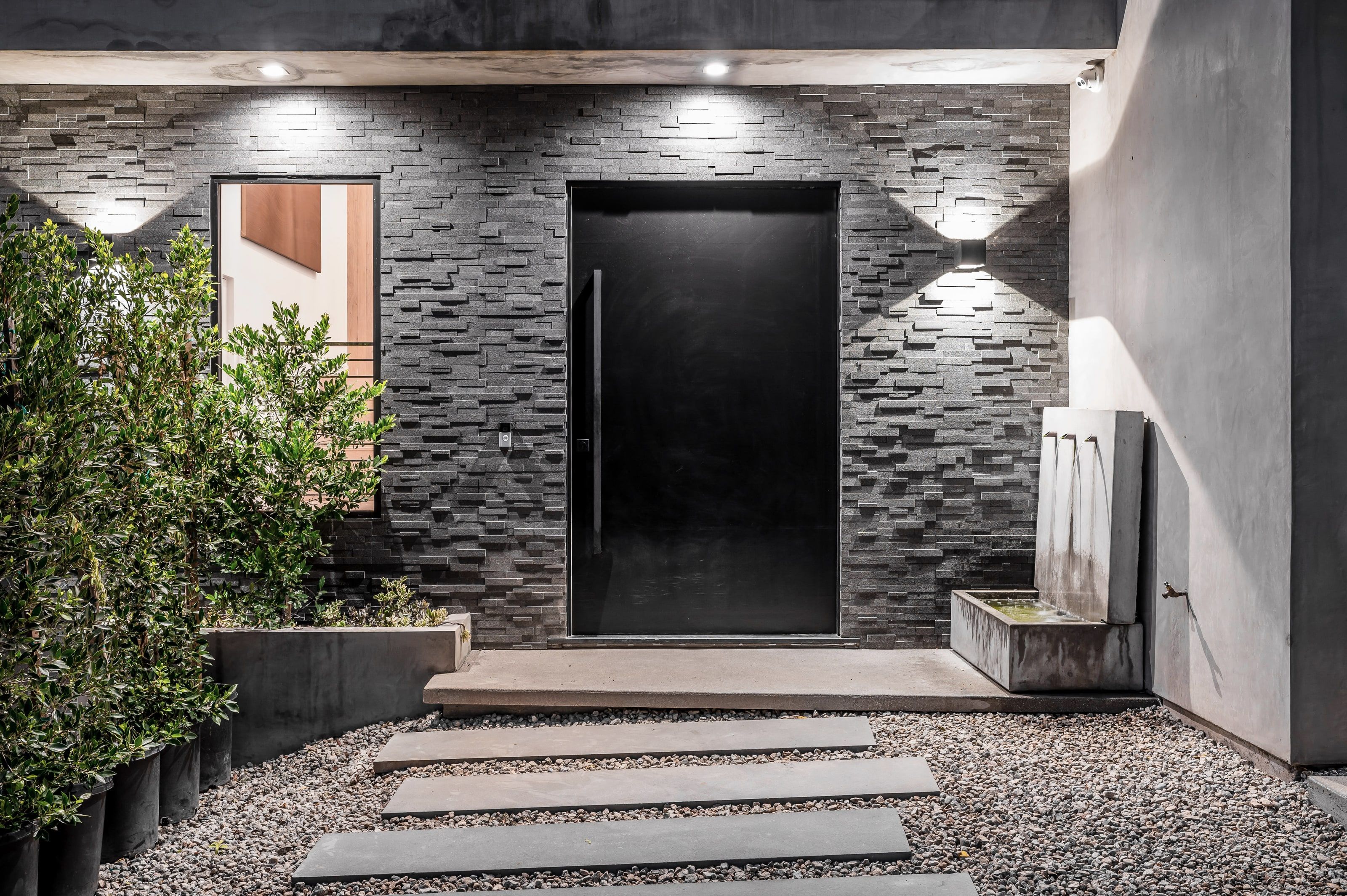 Elegante schwarze Haustür mit Fenster in einer beleuchteten Natursteinfassade bei Nacht